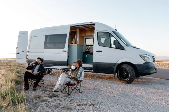 Couple enjoys drinks by their white Mercedes Sprinter rv rental camper van, interior visible at sunset.. Freightliner Sprinter 2017