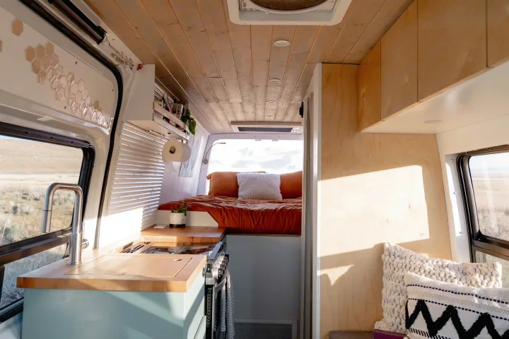 Spacious and bright RV rental interior featuring a modern kitchen with a sink & stove, and a cozy bed, perfect for van life adventures.. Freightliner Sprinter 2017