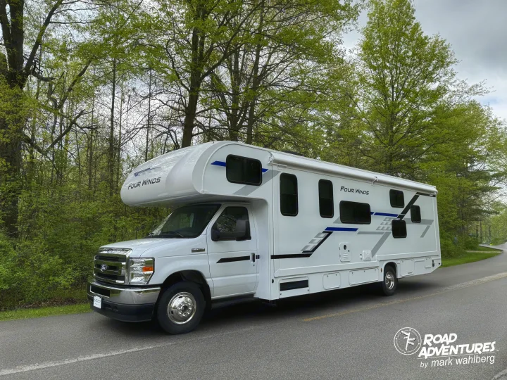 White Four Winds RV rental parked on a paved road, surrounded by fresh green trees, ready for your road adventures.. Thor Motor Coach Four Winds 2026