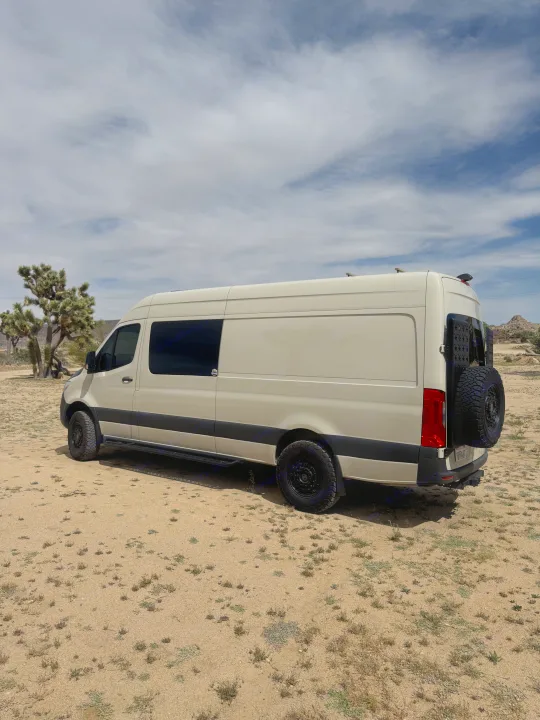 White Sprinter camper van, an RV rental, on a dirt road in the desert, with Joshua trees.. VanCraft VanCraft Class B 2022