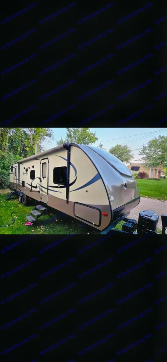 This tan and brown travel trailer RV rental, with its awning extended, is parked on grass and ready for adventure.. Forest River Surveyor 2016