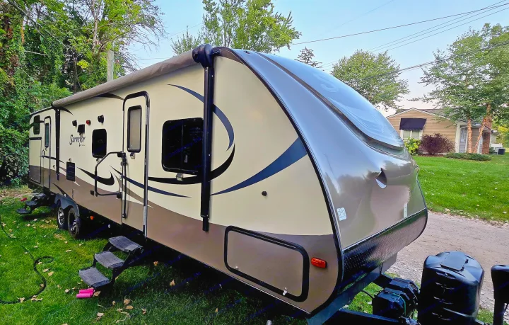 A beige and brown Surveyor travel trailer, parked outdoors on grass, highlighting its features for an RV rental.. Forest River Surveyor 2016