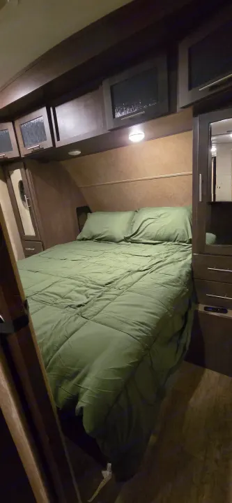 Compact RV rental bedroom featuring a green-sheeted bed, pillows, and built-in wooden cabinetry. Perfect for travel.. Forest River Surveyor 2016