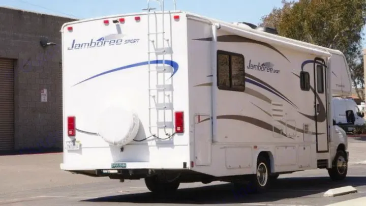 This white Jamboree Sport RV rental is parked, showing its rear and side details, including a ladder and spare tire.. Jamboree Sport 2010