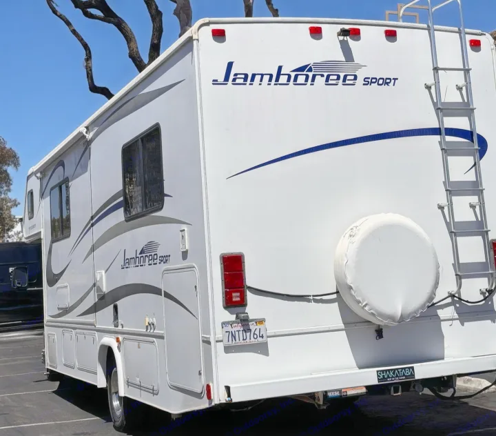 White Jamboree Sport RV rental, a motorhome with blue/grey decals and a rear ladder, ready for your next adventure.. Jamboree Sport 2010