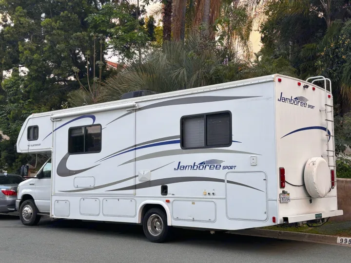 White Fleetwood Jamboree Sport RV rental, with an awning and ladder, parked on a street among trees.. Jamboree Sport 2010