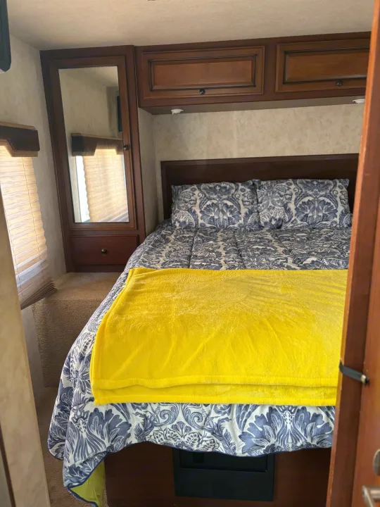 Inside an RV rental: a compact bedroom with blue & white patterned bedding, yellow blanket, wooden cabinets & mirror.. Jamboree Sport 2010
