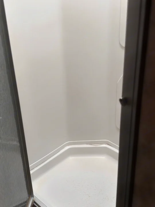 A clean, compact hexagonal shower stall inside an **rv rental**. View through an open door, showing white walls & base.. Jamboree Sport 2010
