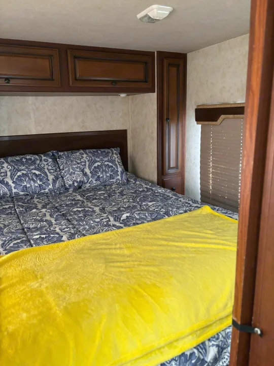 Cozy RV rental bedroom with patterned bed, bright yellow blanket, and ample wooden cabinetry.. Jamboree Sport 2010
