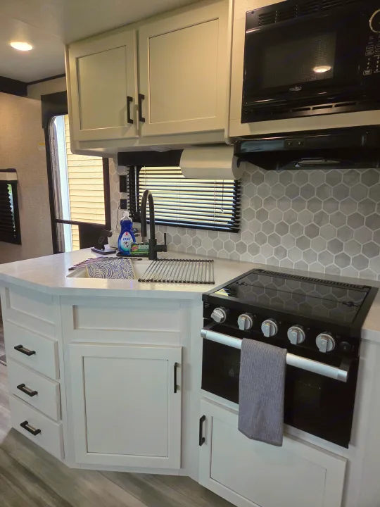 RV rental kitchen featuring white cabinets, black microwave & stove, hexagon backsplash, sink, and drying rack.. Jayco Jay Flight 2024