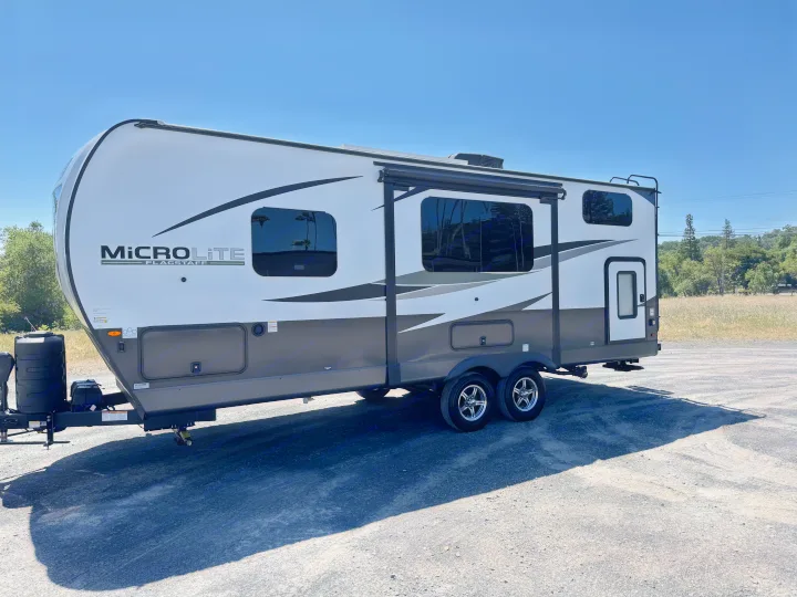 White & gray Micro Lite travel trailer. Ideal RV rental unit, parked on gravel under a sunny sky.. Flagstaff Micro Lite 25DBH 2025