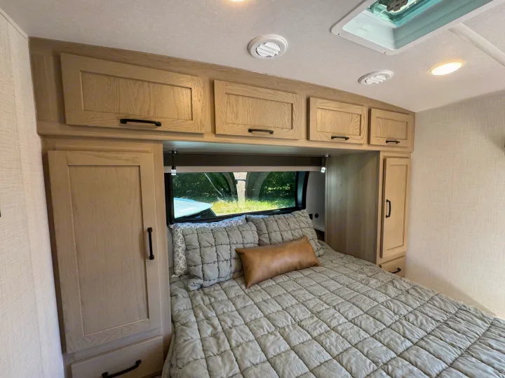 This RV rental's bedroom offers a comfortable bed, ample cabinet storage, and a view of nature. Ideal for travel.. Flagstaff Micro Lite 25DBH 2025