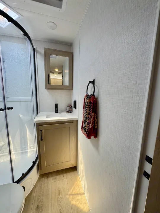 RV rental bathroom features a compact shower, vanity, sink, mirror, and a decorative towel on the wall. Light wood floors.. Flagstaff Micro Lite 25DBH 2025