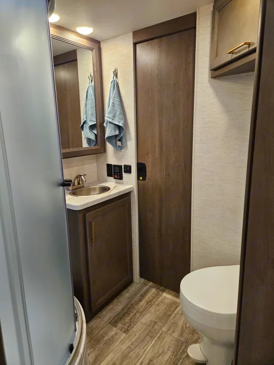 Modern, compact rv rental bathroom featuring a vanity, sink, mirror, toilet, and frosted shower door.. Thor Chateau 2024