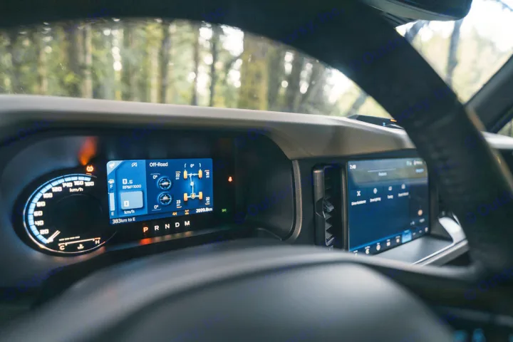 Digital dashboard of an RV rental, showing off-road info (0 km/h, 4H, 2699.8m) and infotainment screen. Trees outside.. Ford Bronco 2024