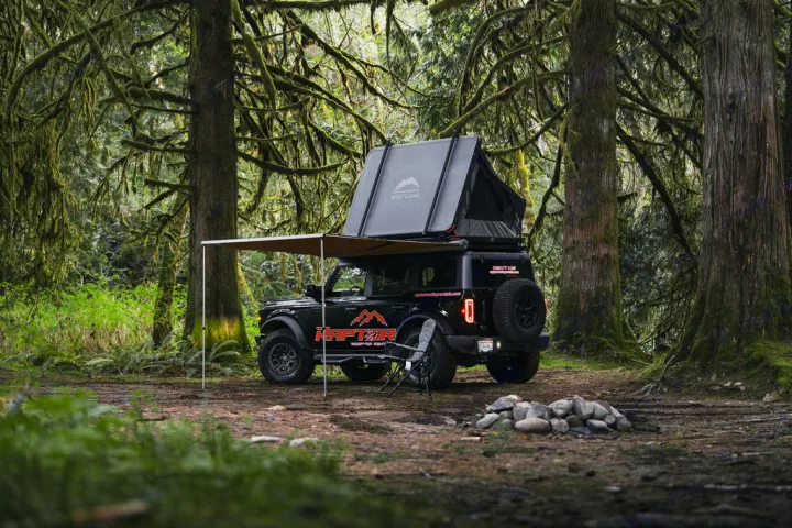 Black Ford Bronco with rooftop tent & awning in a mossy forest clearing. Your ideal rv rental for overlanding adventures.. Ford Bronco 2024