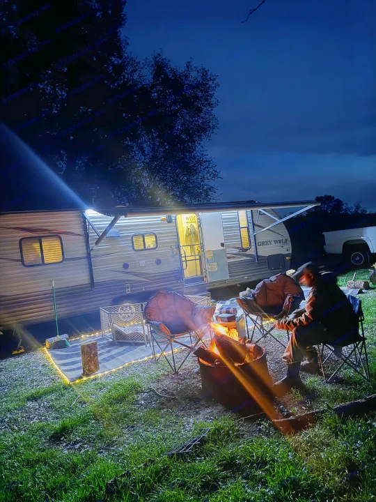 Nighttime comfort at an RV rental campsite: campers gathered around a glowing fire next to their illuminated travel trailer.. Forest River Cherokee Grey Wolf 2016
