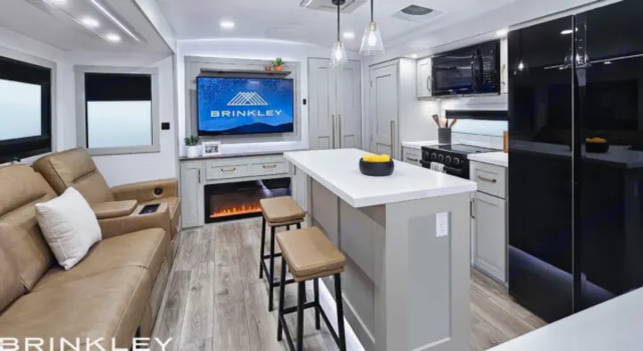 Modern RV rental interior: spacious living area with recliners, TV/fireplace, and a stylish kitchen island with bar stools.. Brinkley Air 295 2025