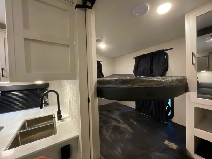 Explore this modern RV rental's interior: a compact kitchen with sink and light cabinets, and cozy bunk beds with dark curtains.. Jayco Eagle Super Lite 2025