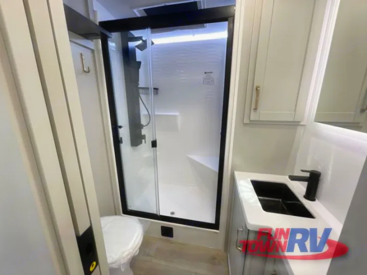 An RV rental's compact bathroom: sleek shower, toilet, and contemporary vanity with black faucet and sink.. Brinkley Air 295 2025
