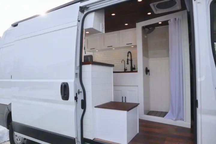 White camper van interior for RV rental. Features a modern kitchen, compact shower, and smart storage solutions.. Dodge Ram 1500 2019