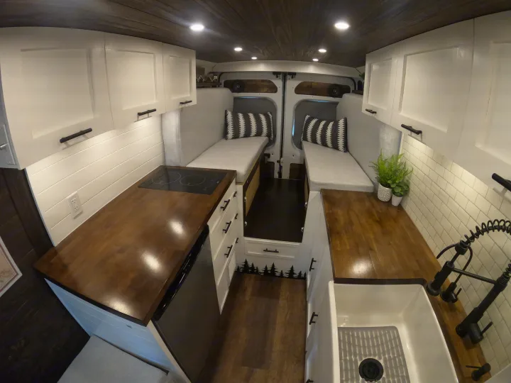 Cozy and functional RV rental interior: wood & white kitchen, dual bench seating/beds, overhead storage, and warm lighting.. Dodge Ram 1500 2019