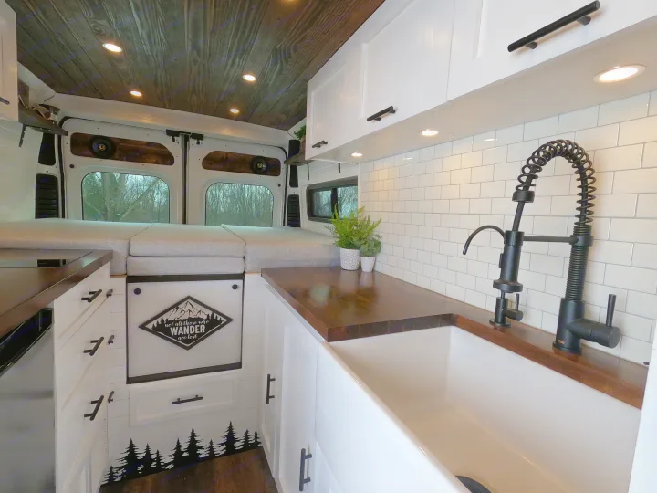Inside a stylish RV rental camper van: white kitchen with a farm sink, wood counters, and gray bedding for a comfortable road trip.. Dodge Ram 1500 2019