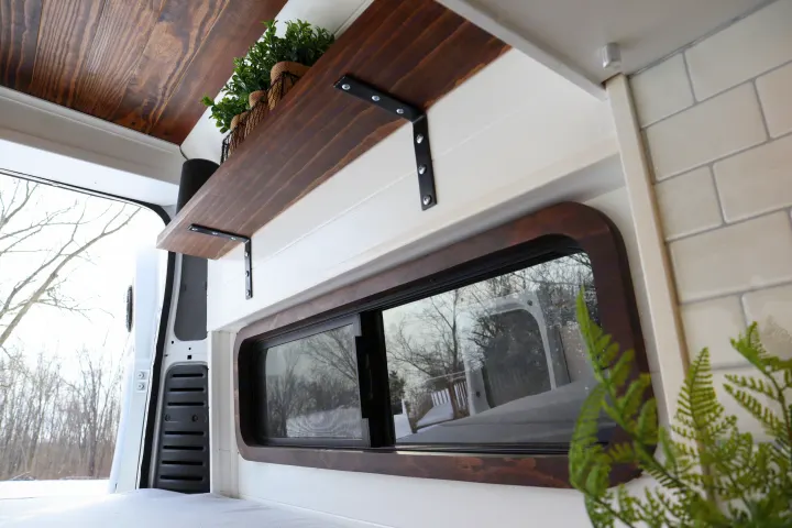 Cozy wood and white camper van rental interior with a custom shelf and snowy window view.. Dodge Ram 1500 2019
