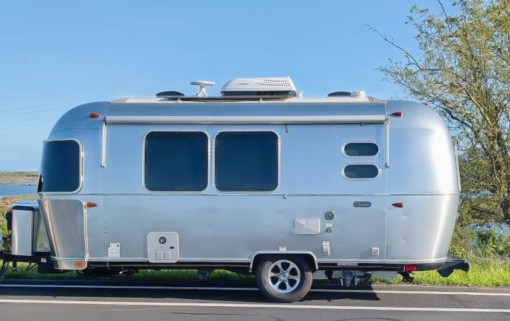 A gleaming silver Airstream Caravel travel trailer (rv rental) by marshland under a blue sky, ready for adventure.. Airstream Caravel 2023