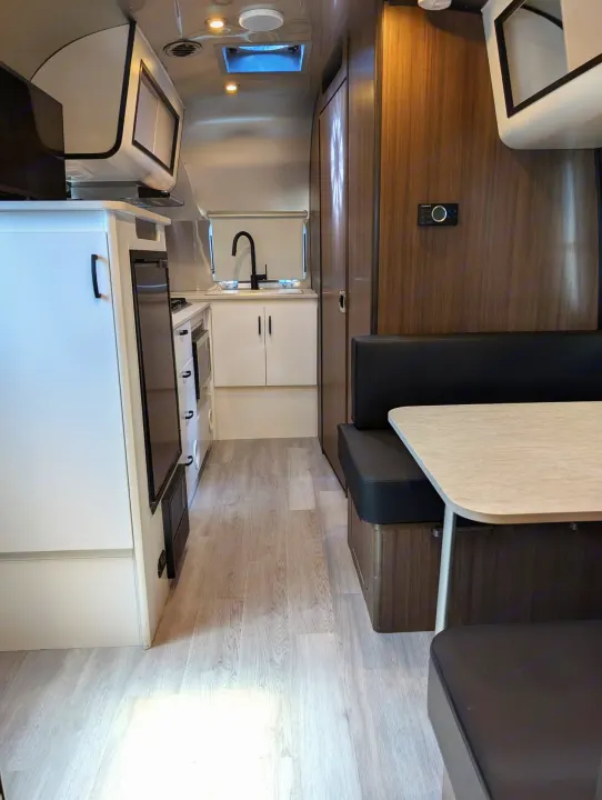 This rv rental's sleek interior features a modern kitchen, black dining booth, and light flooring. Ideal for comfortable travel.. Airstream Caravel 2023