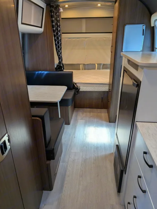RV rental interior showcasing a cozy dining booth, bed, and compact kitchen area with light wood flooring.. Airstream Caravel 2023