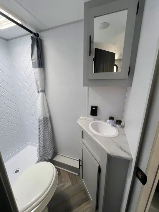 Compact RV rental bathroom featuring a shower, toilet, sink vanity, and mirrored medicine cabinet.. Forest River Salem FSX 2021