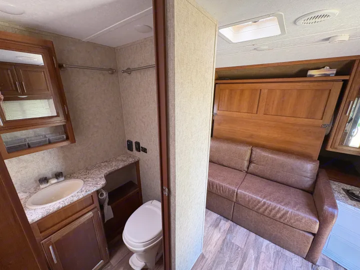 RV rental interior: a compact bathroom with a sink, toilet, and a cozy living area featuring a brown sofa that converts to a bed.. Tracer Tracer Air 2017
