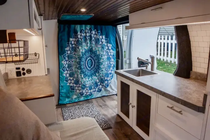 Modern RV rental interior with a compact kitchen, comfortable bed area, and a blue mandala curtain at the rear. Ideal for mobile living.. Chevrolet Express 3500 2012