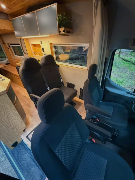 Spacious RV rental camper van interior. Features front & rear seating, overhead storage, and windows overlooking a serene forest.. Ford Transit 2023