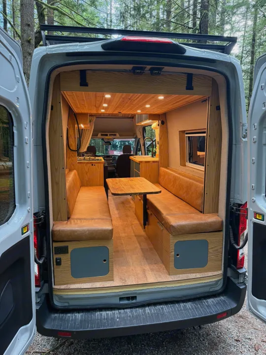 Cozy custom camper van interior perfect for an RV rental adventure, featuring benches, kitchen, & warm lighting.. Ford Transit 2023