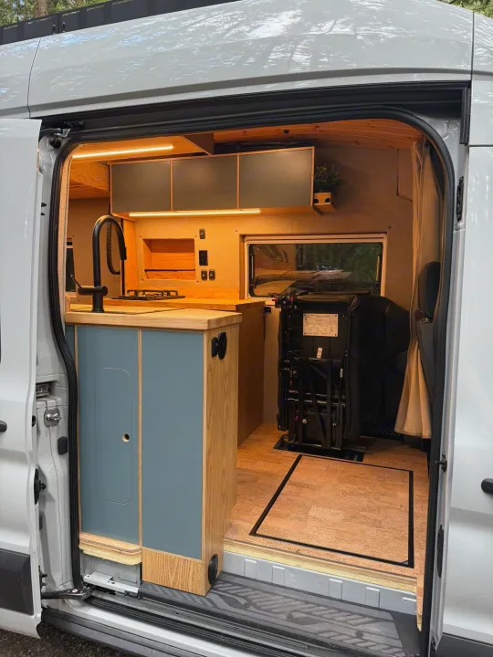 Modern camper van interior with custom kitchen (blue cabinets, sink) and versatile track seating, great for your RV rental journey.. Ford Transit 2023