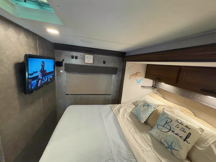 Comfortable RV rental bedroom, featuring a TV, bed with beach pillows, and window shade, offering a relaxing stay.. Forest River Sunseeker LE 2021