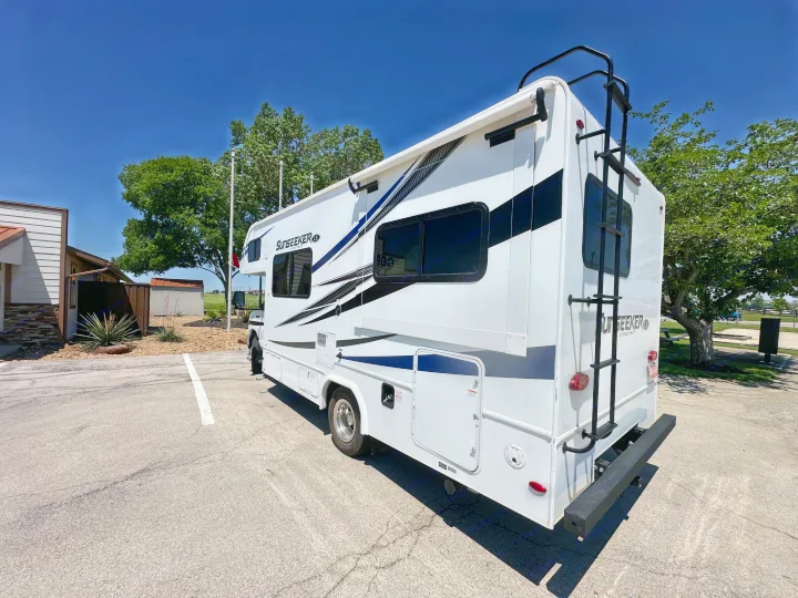A white Sunseeker RV, ideal for an rv rental, is parked outdoors on asphalt with trees under a clear blue sky.. Forest River Sunseeker LE 2021