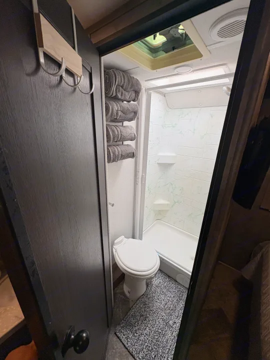 This RV rental's compact bathroom features a white toilet, stand-up shower, and wall-mounted towel storage.. Forest River Sunseeker LE 2021
