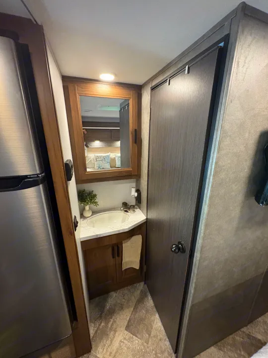 Compact and functional RV rental interior featuring a modern bathroom vanity, kitchen fridge, and bedroom access.. Forest River Sunseeker LE 2021