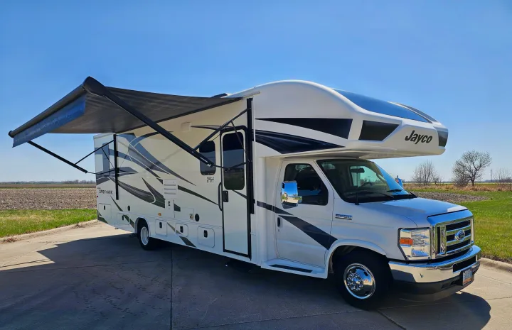 White Jayco Greyhawk Class C RV with an extended awning, parked outdoors. Perfect for your next rv rental adventure.. Jayco Greyhawk 2023