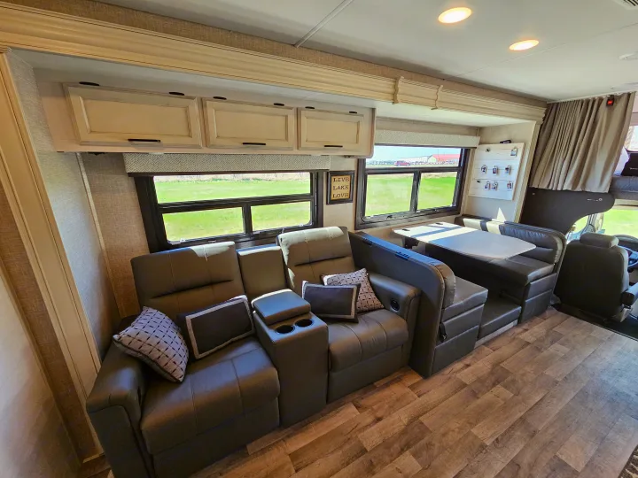Inviting motorhome RV rental interior: gray recliners, dinette, overhead cabinets, wood flooring, scenic views.. Jayco Greyhawk 2023