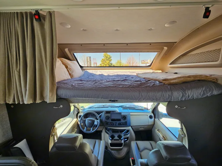 Inside an RV rental: a cozy cab-over bunk bed sits above the spacious driver's cockpit for your next adventure.. Jayco Greyhawk 2023