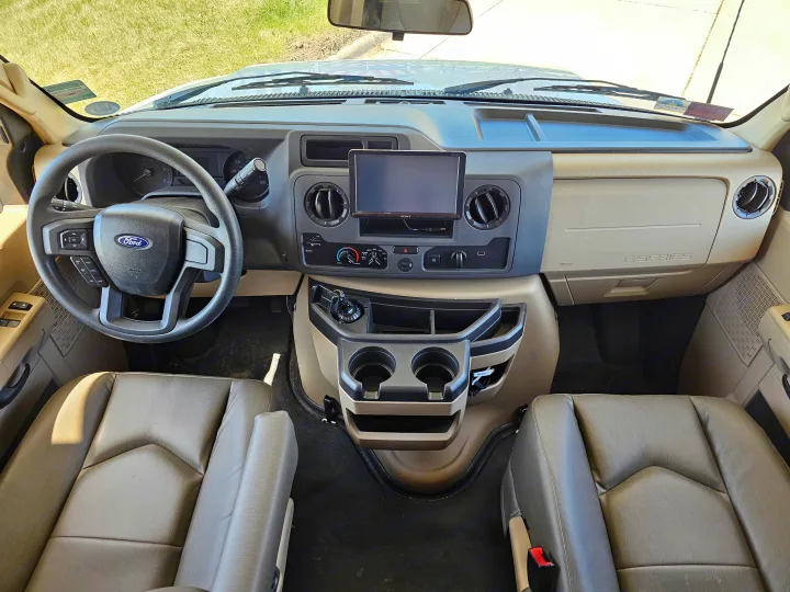 Inside an RV rental: Full front view of the vehicle's dashboard, steering wheel, and tan bucket seats.. Jayco Greyhawk 2023