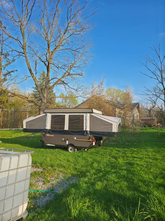 Pop-up camper (RV rental) set up in a grassy spring yard, surrounded by trees and a clear sky.. Forest River Rockwood LTD 2024
