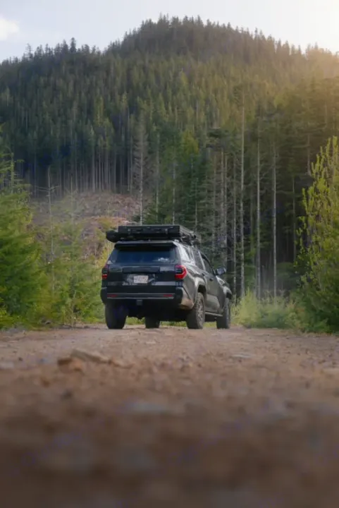 Black SUV with rooftop tent on a dirt forest road between tall pines. Imagine this outdoor exploration with an RV rental.. Toyota 4Runner 2025