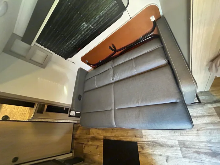 Relax in your RV rental! Comfy gray dinette sofa with a brown backrest, wood-look floor, and black window shade.. 4YDTCMH25RJ935536 1805RB 2024