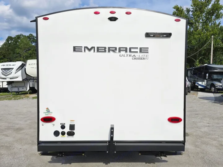 Rear of a white Embrace Ultra-Lite travel trailer, ready for RV rental. Shows utility hookups and red tail lights.. Cruiser Embrace EL26RB 2024