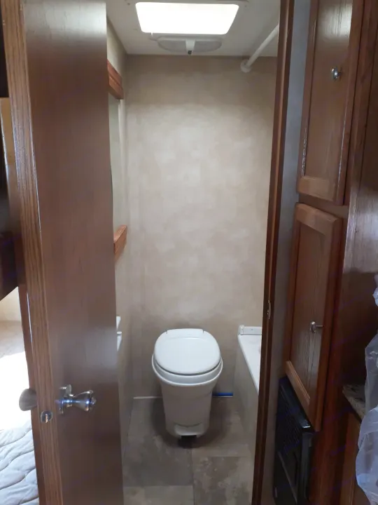Inside an RV rental bathroom, featuring a white toilet, small tub, and built-in wooden cabinets.. Coachmen Clipper 2013